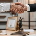 Close-up of a handshake between two professionals in a modern office setting, emphasizing partnership and agreement.